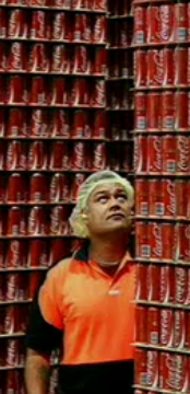 A screengrab of a Coca-Cola employee looking up a pallet of Coke Classic cans.